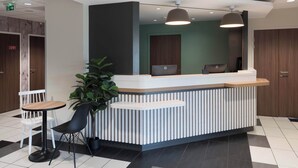A reception desk with a modern design, including a white and grey color scheme, a potted plant, and a seating area with a table and chairs. - B&B HOTEL Laval Ouest (Laval)