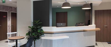 A reception desk with a modern design, including a white and grey color scheme, a potted plant, and a seating area with a table and chairs.