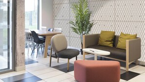 A modern waiting area with a sofa, chairs, a dining table, and a potted plant. - B&B HOTEL Laval Ouest (Laval)