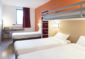 Ein Hotelzimmer mit zwei Betten, einem Schreibtisch, einem Stuhl und einem fensterbelaubten Fenster.