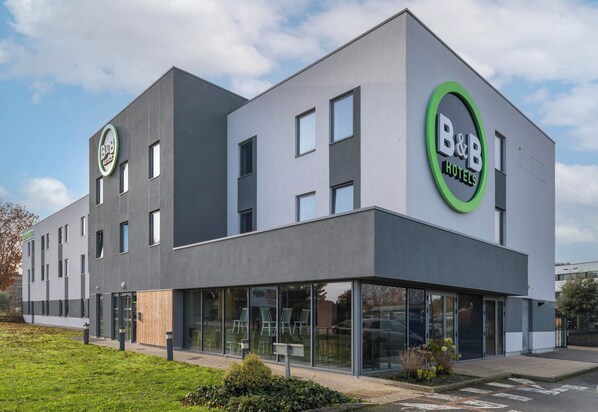 Ein modernes Bed and Breakfast Hotel mit schlichter Fassade, großen Fenstern und einem grünen, kreisförmigen Logo.