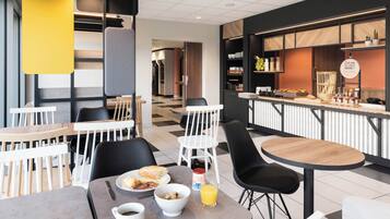A modern cafe with tables and chairs, a breakfast spread, and a counter with food items.