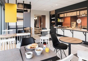Un café moderno con mesas y sillas, una bandeja de desayuno y una barra con alimentos.
