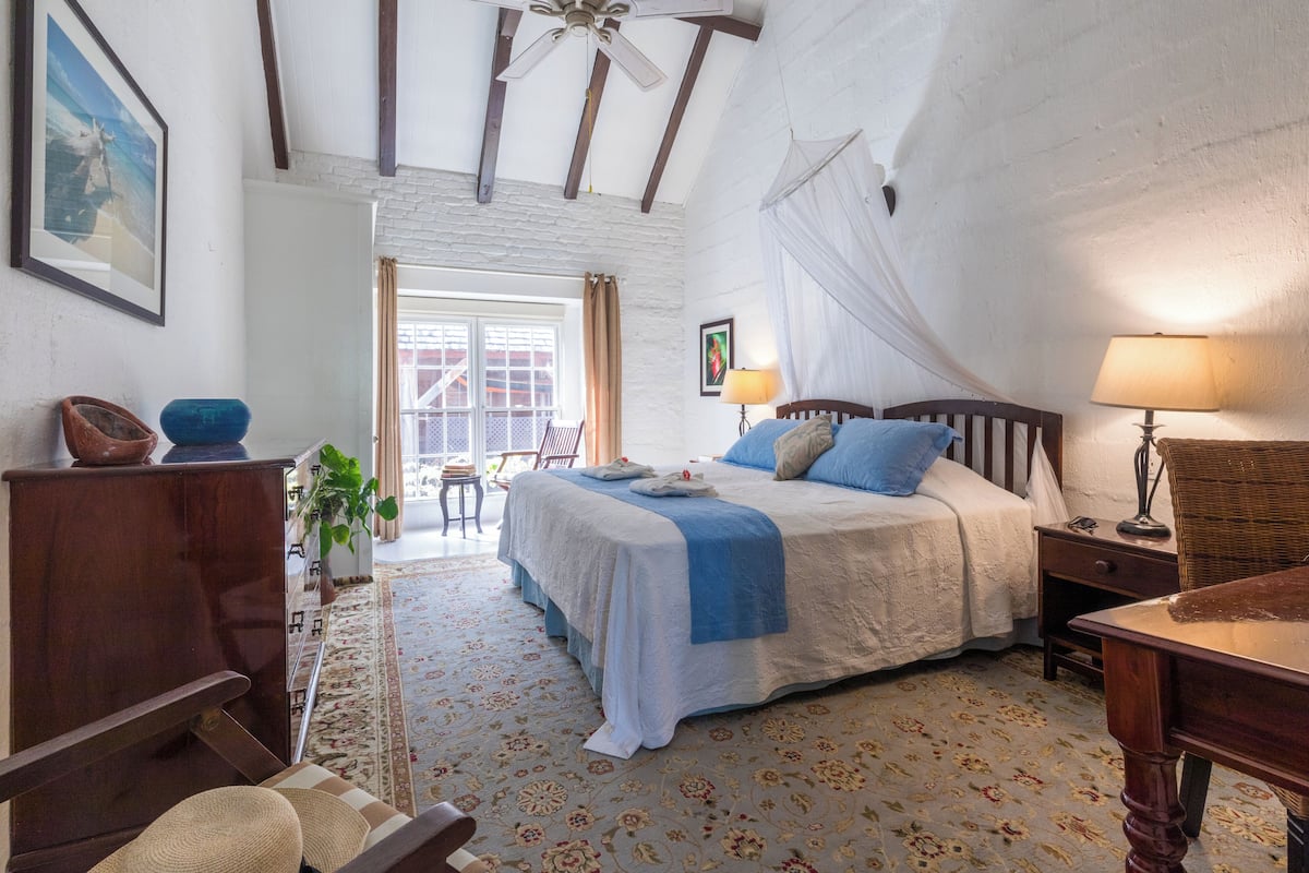A bedroom with a large bed, a wooden nightstand, a wicker chair, and a desk.