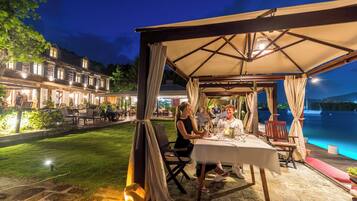 An outdoor dining area with a covered pavilion, stone flooring, and a view of a body of water.