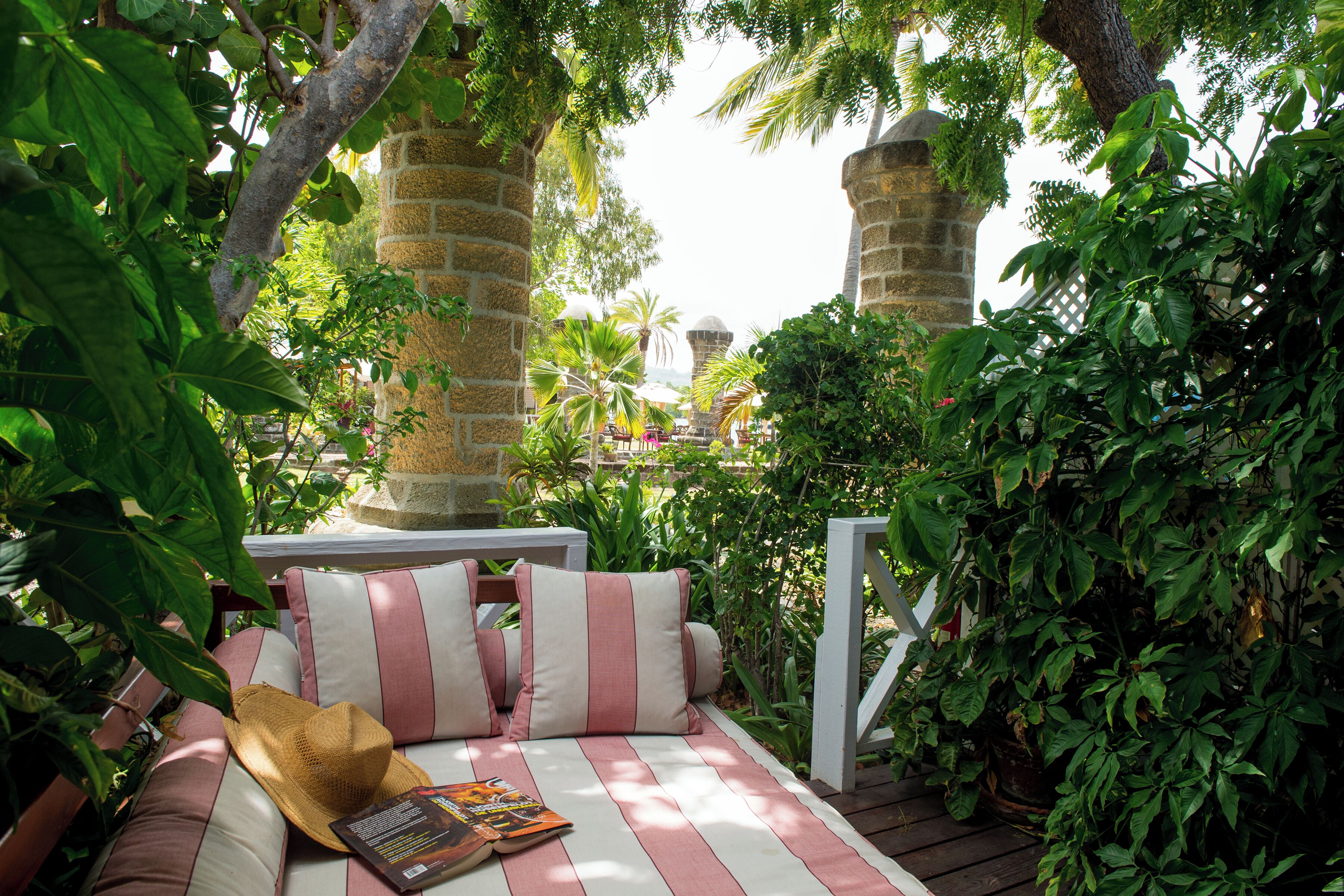 A cozy outdoor seating area with a cushioned bench, a straw hat, and a book.