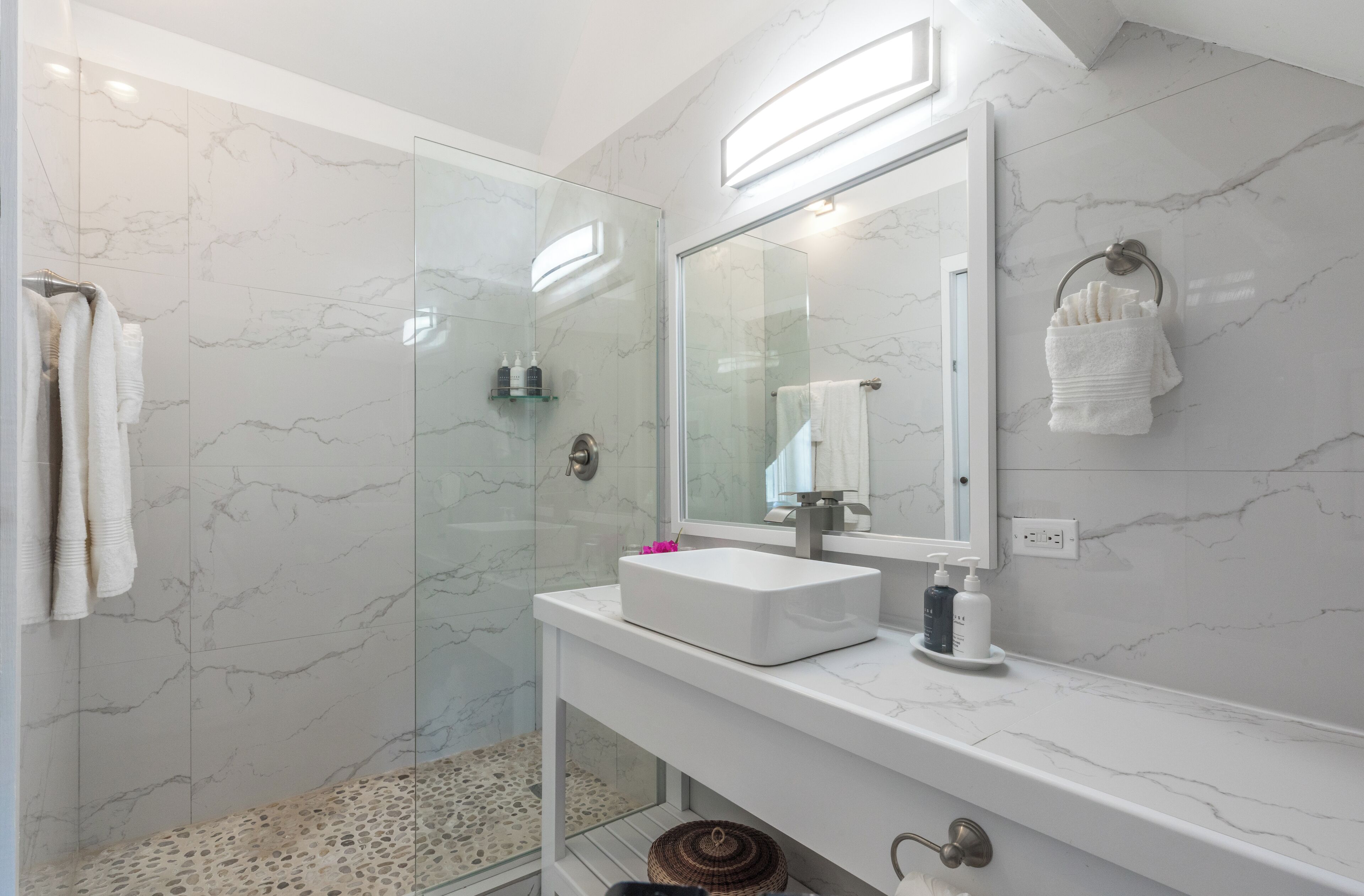 A modern bathroom with a glass shower enclosure, a white sink, and a large mirror.