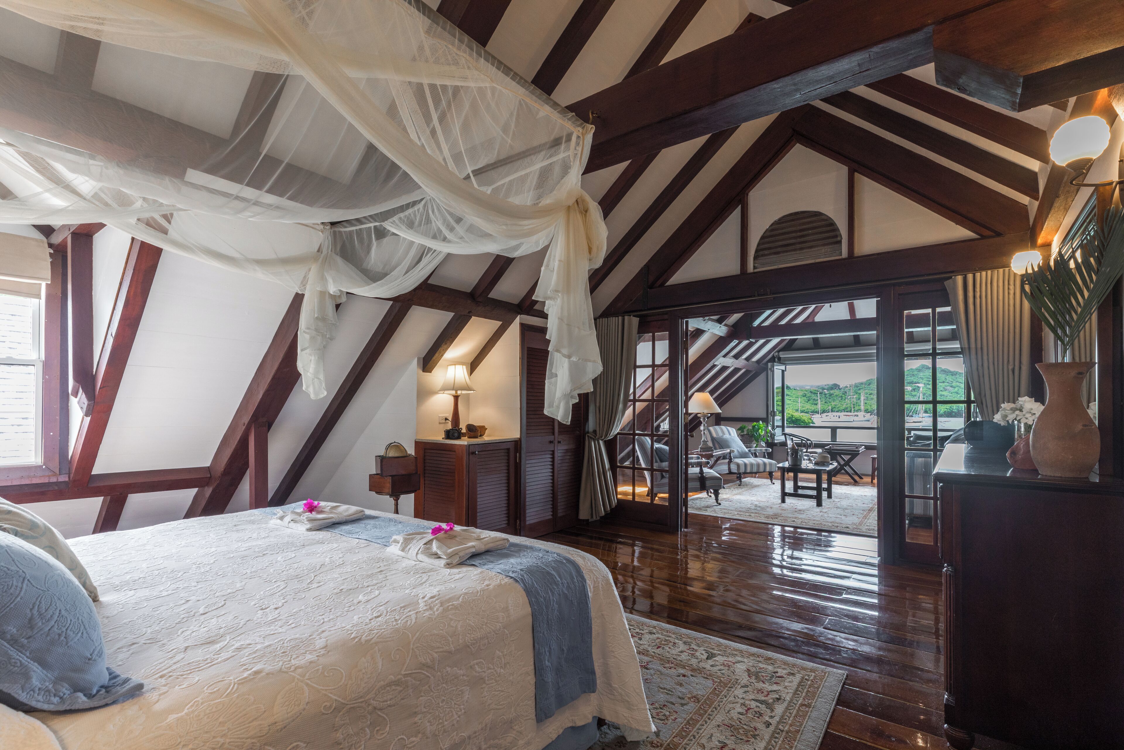 Een slaapkamer met een groot bed, houten balken, een hemelbed en uitzicht op het omliggende landschap.