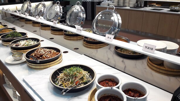 Un buffet proposant divers plats et accompagnements, notamment une salade, des nouilles et des sauces.