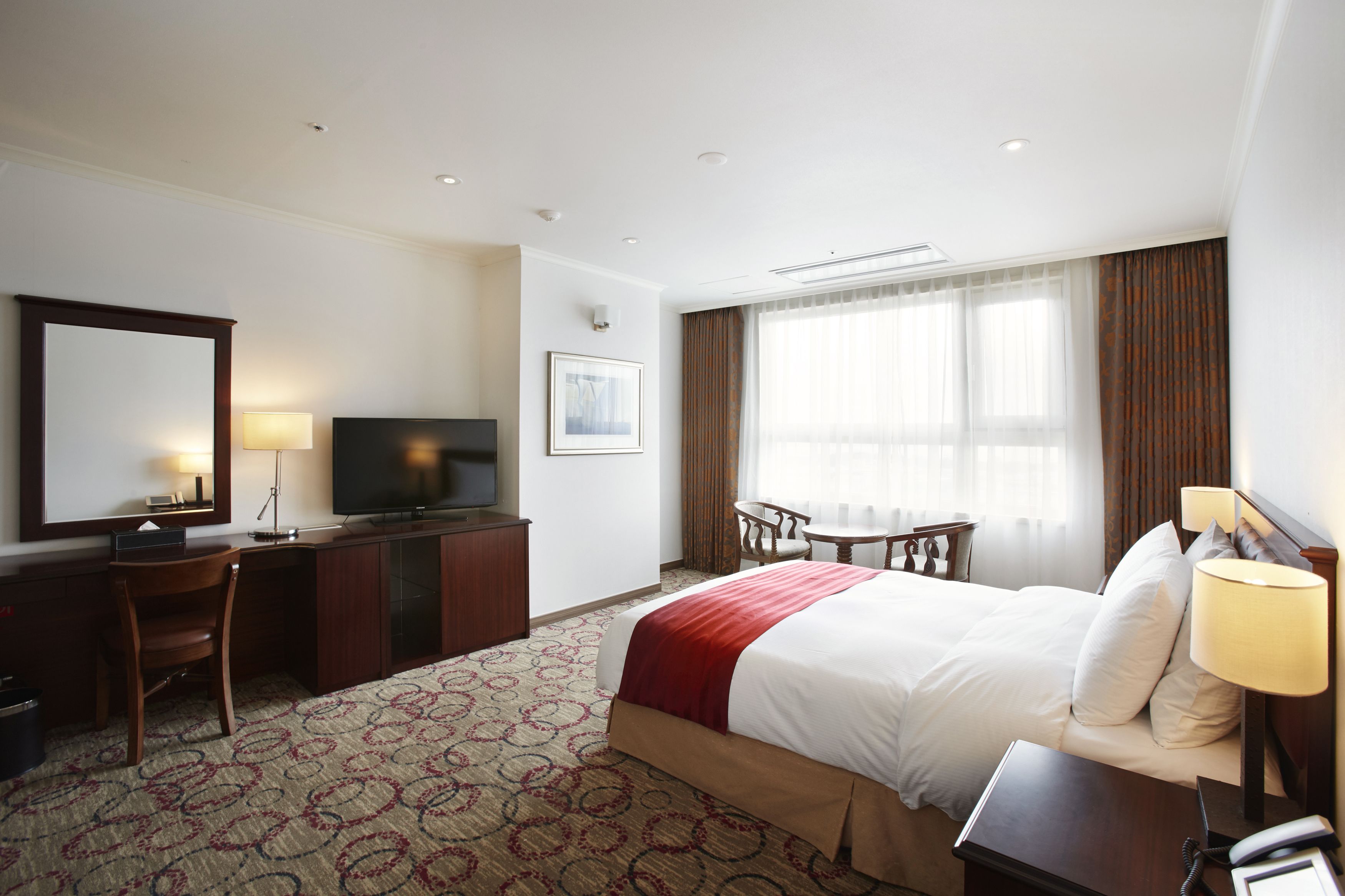 Una habitación de hotel con cama, escritorio, televisor y ventana con cortinas.