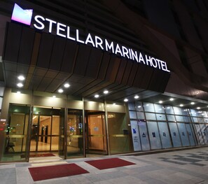 Das Äußere des Stellarl Marina Hotels mit einer markanten, beleuchteten Signatur, Glastüren und einem gefliesten Eingangsbereich.