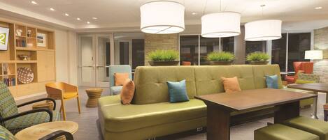 A modern lounge area with a green sofa, wooden chairs, a dining table, and pendant lighting.