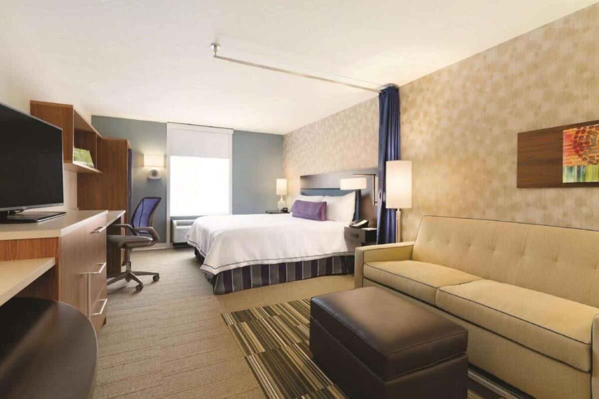 A hotel room with a bed, a desk, a chair, a sofa, and a television.