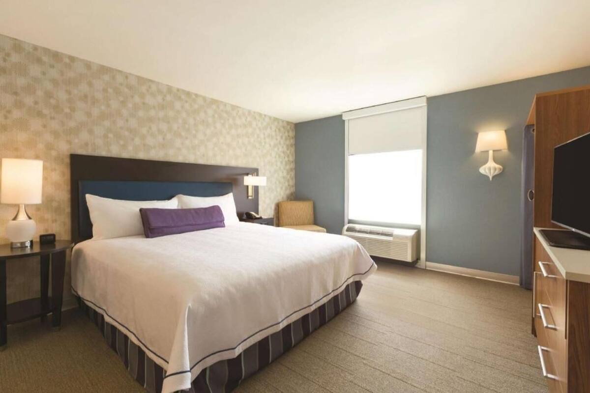Une chambre d’hôtel avec un lit, des tables de chevet, une télévision, une lampe et une fenêtre.