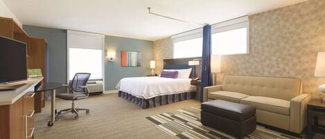 A hotel room with a bed, a sofa, a desk with a computer, a chair, and a TV.