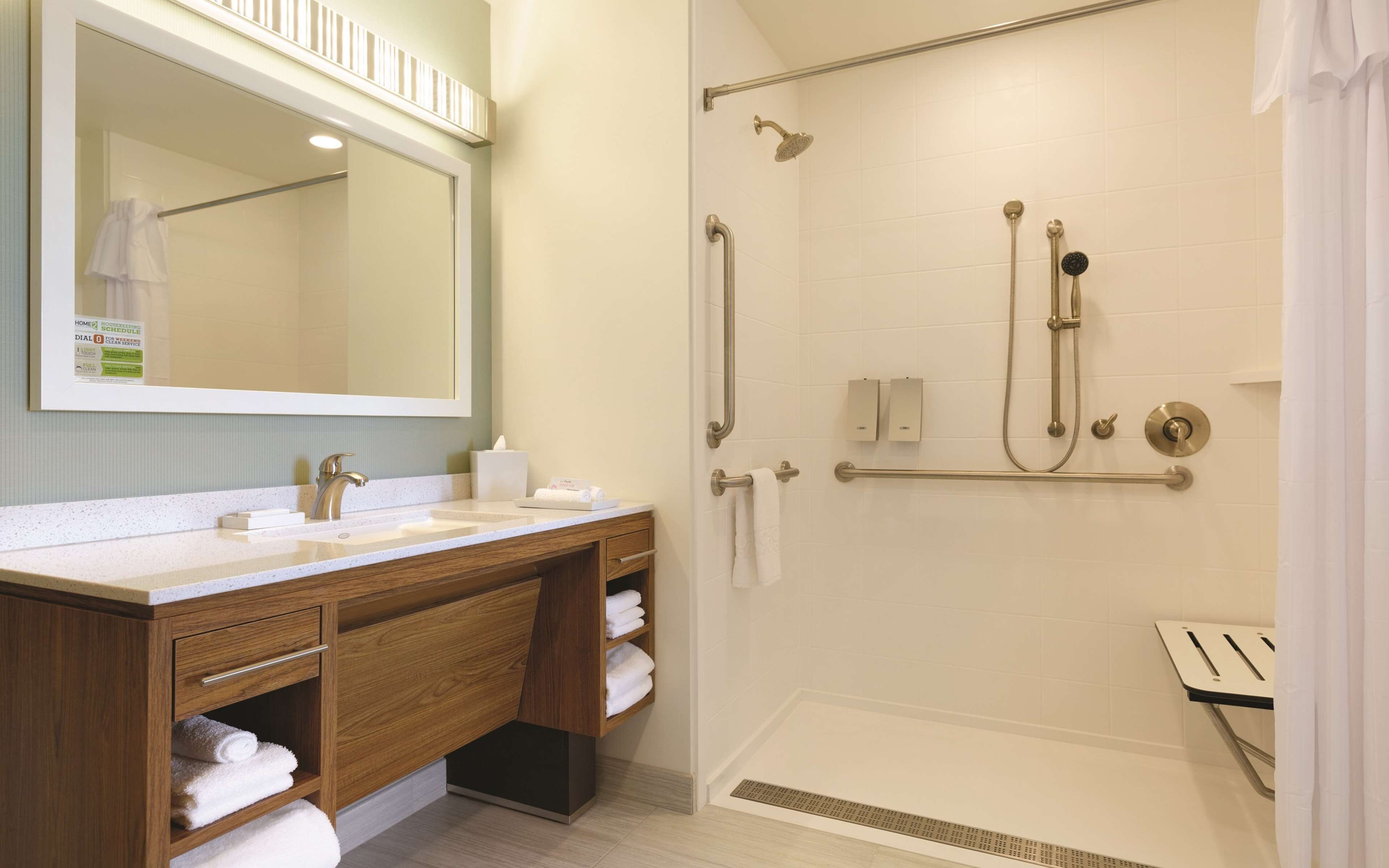A modern bathroom with a wooden vanity, a large mirror, a shower with a handheld showerhead, and a towel rack.