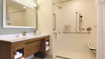 A modern bathroom with a wooden vanity, a large mirror, a shower with a handheld showerhead, and a towel rack.