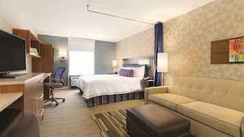 Una camera d'albergo con un letto, un divano, una scrivania con un computer, una sedia e una televisione.