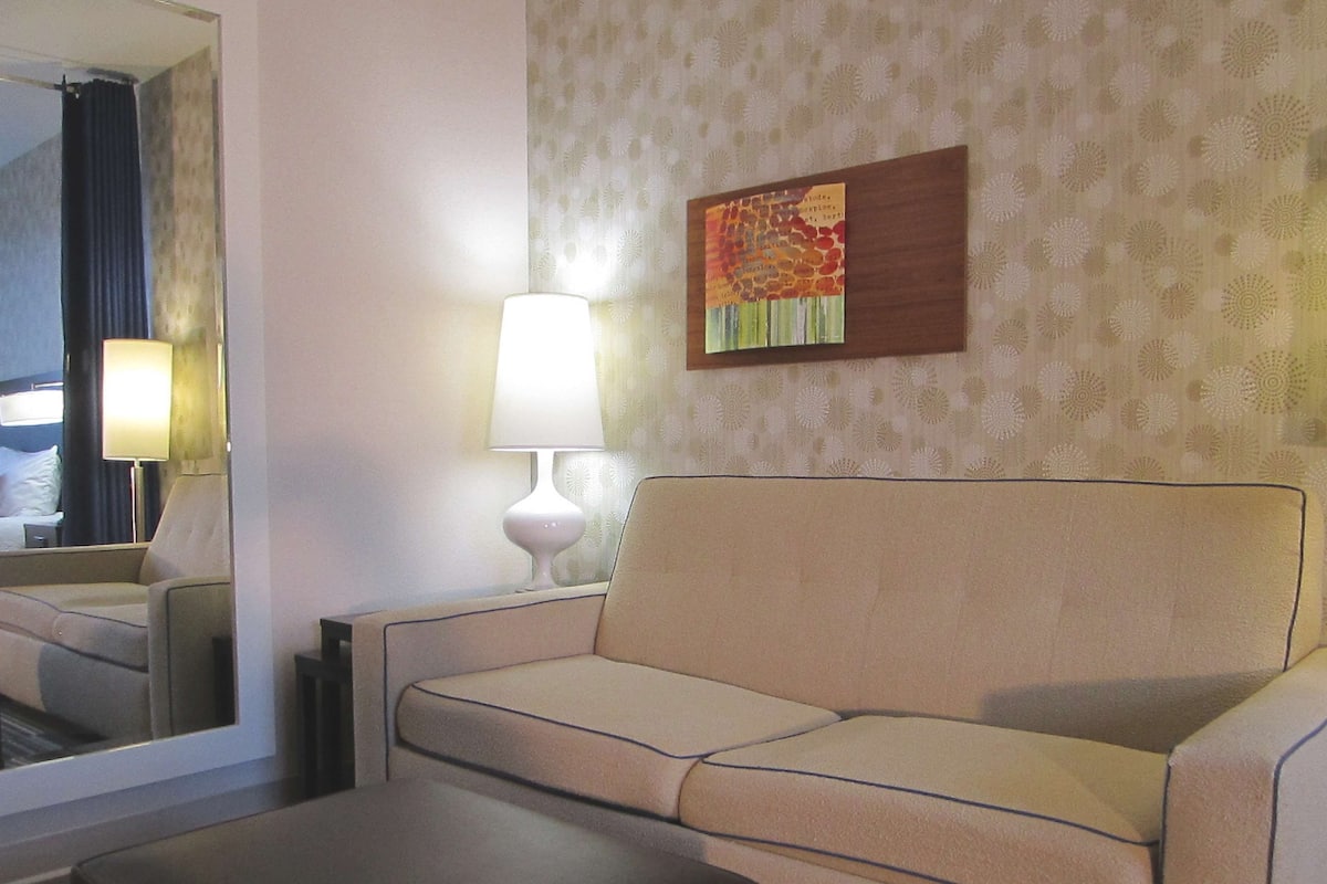 Une chambre d’hôtel avec un canapé, une petite table, une lampe et un tableau au mur.