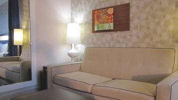A hotel room with a sofa, a small table, a lamp, and a painting on the wall.