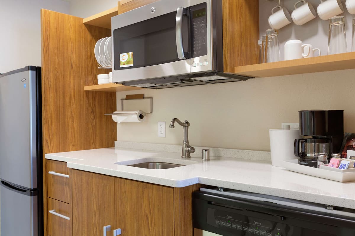 Une cuisine moderne équipée d’un réfrigérateur en acier inoxydable, d’un four à micro-ondes, d’un lave-vaisselle et de meubles de rangement en bois.