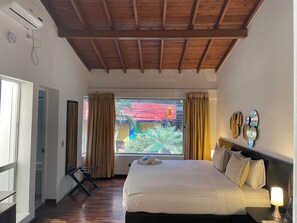 A hotel room with a bed, a bedside lamp, a window with curtains, a wooden ceiling, and a view of the outside. - Hostal Lleras Calle 8 - Hostel (Medellín)