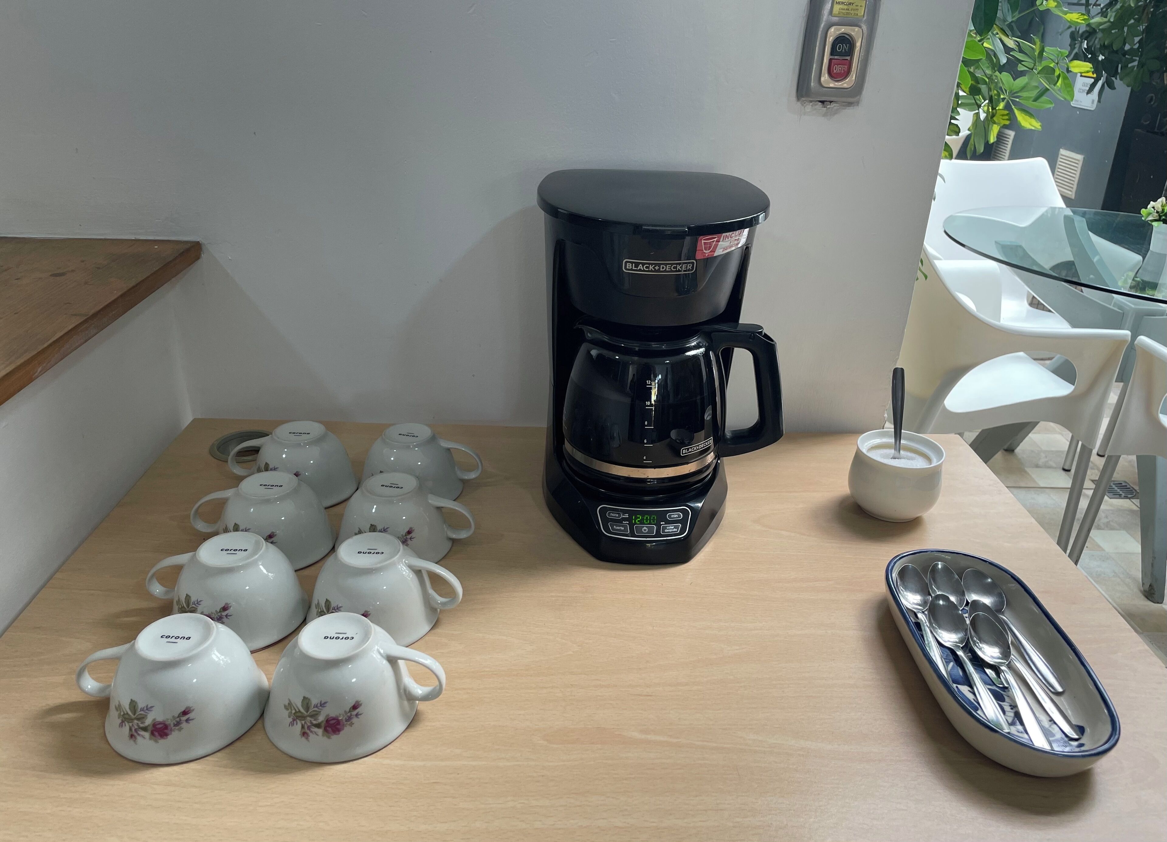 Una cafetera, teteras y un bol de cucharas sobre una mesa.