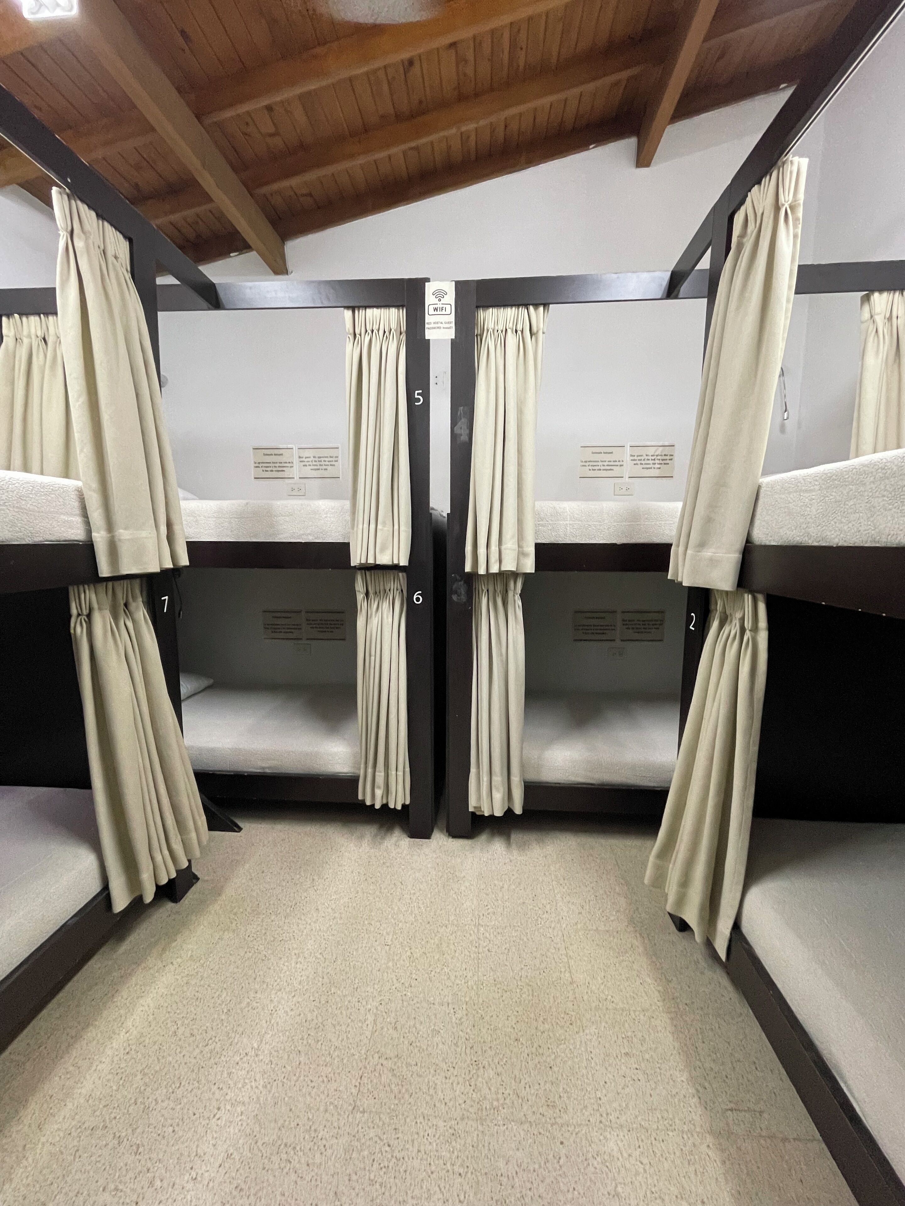 A bunk room with four beds, each with a curtain. There is a sign indicating a WiFi connection.