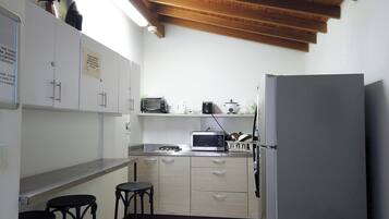Cocina compacta con microondas, tostadora y refrigerador. Hay dos taburetes y un lavamanos.
