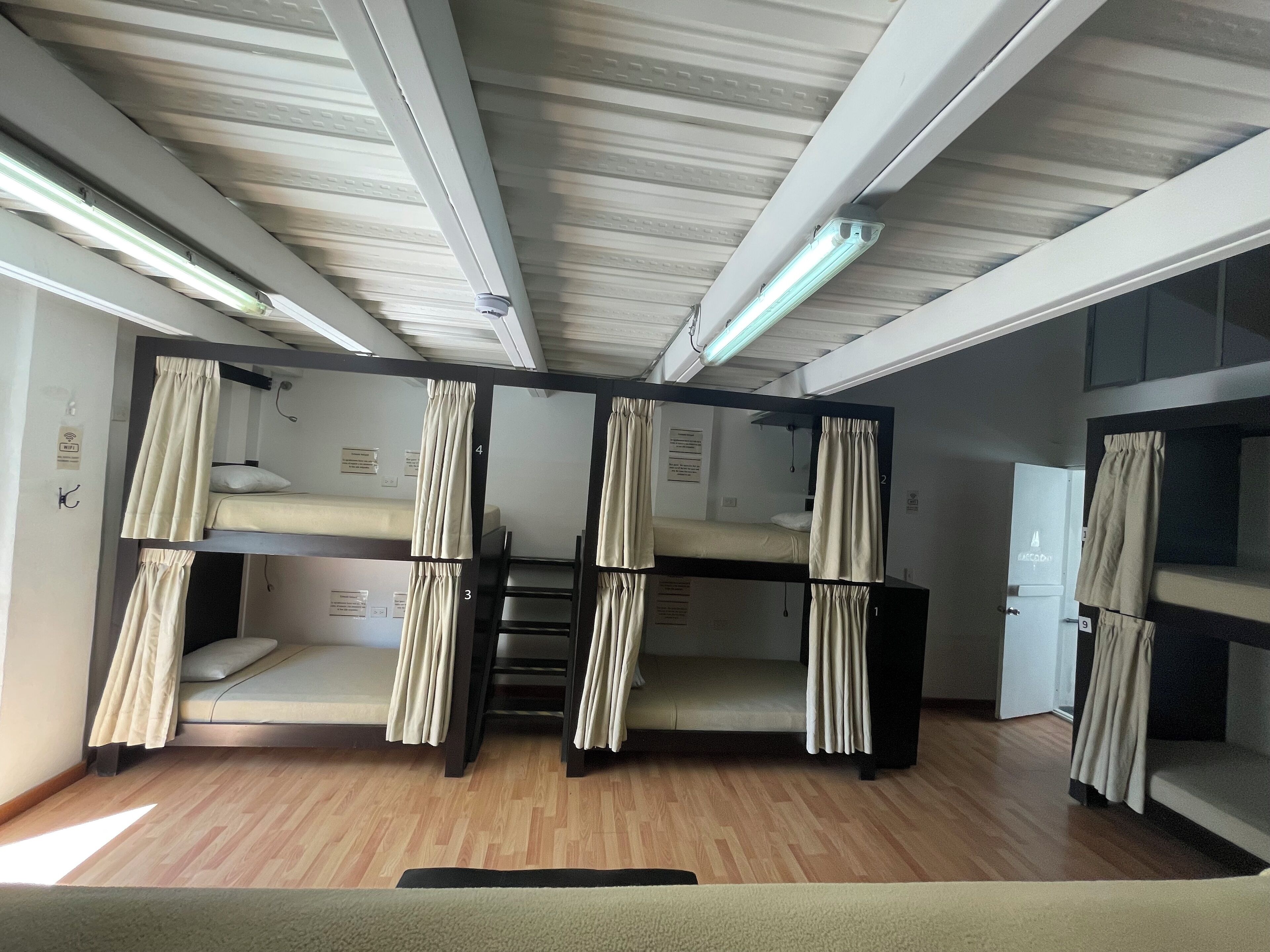 A dormitory room with bunk beds, wooden flooring, and ceiling lights.