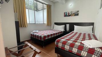 A hotel room with two beds, a desk, a chair, a large window with curtains, and a ceiling fan.