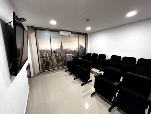 Un salón de conferencias con vista a la ciudad, sillas negras, un televisor de pantalla plana y un equipo de aire acondicionado.