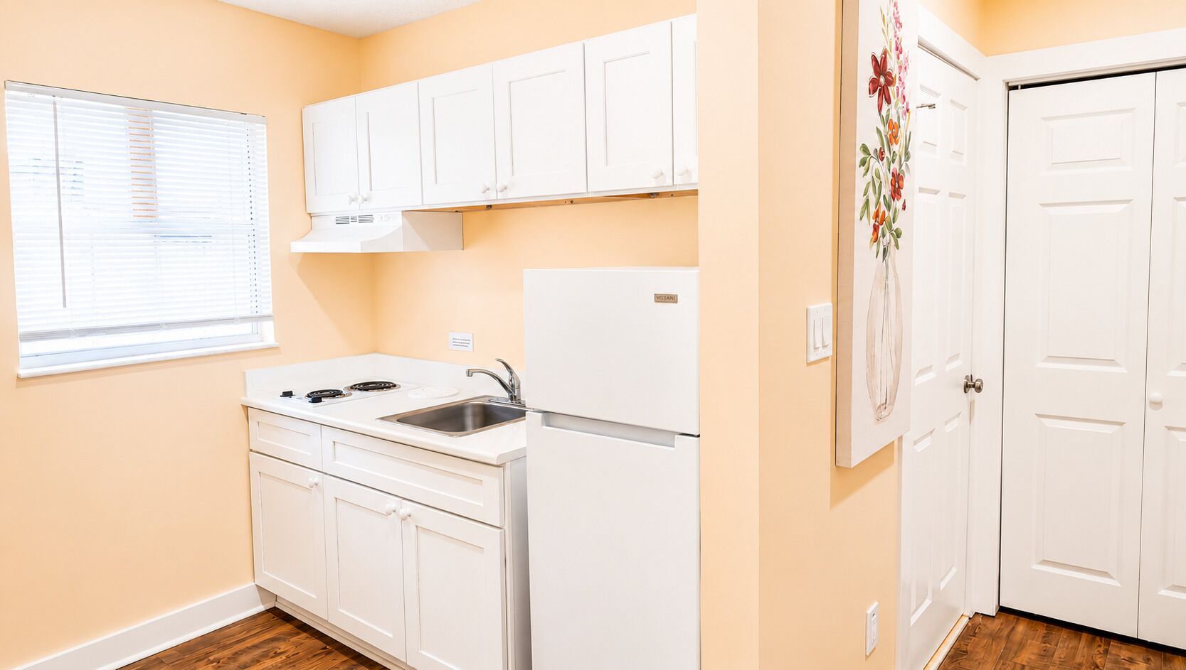 A kitchen with white cabinets, a refrigerator, a sink, and a window with blinds.