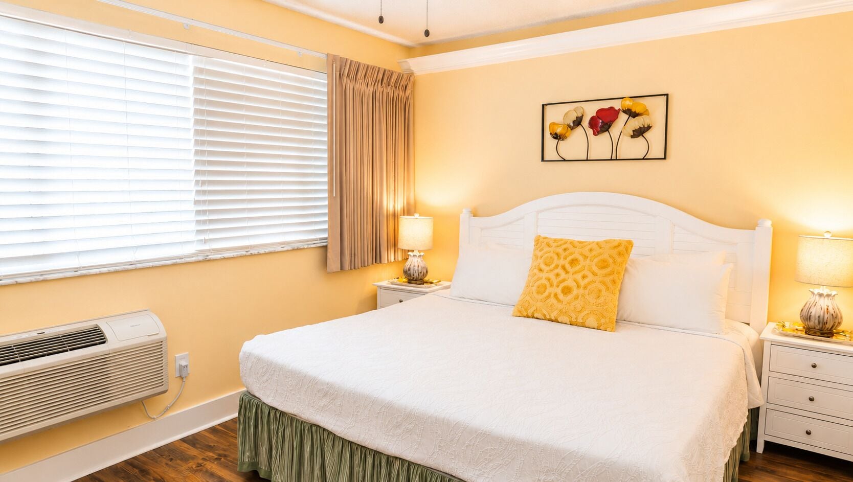 A bedroom with a bed, bedside tables, a lamp, a wall art piece, and an air conditioning unit.