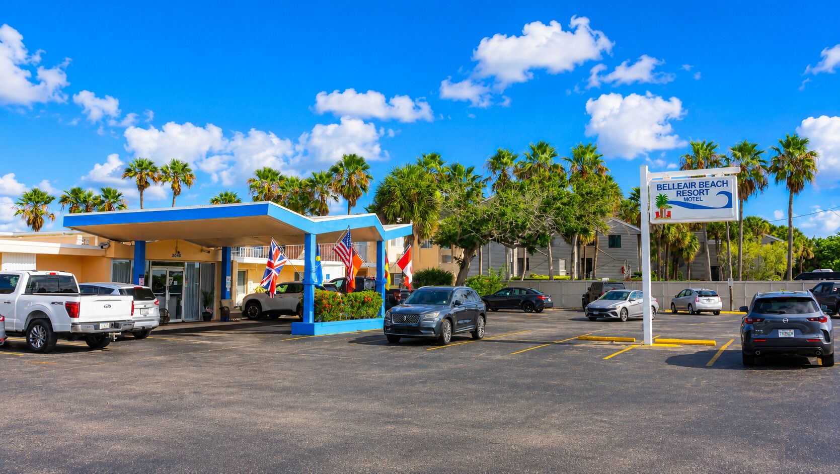 Un motel avec un auvent bleu, plusieurs drapeaux et un ciel d’un bleu limpide.