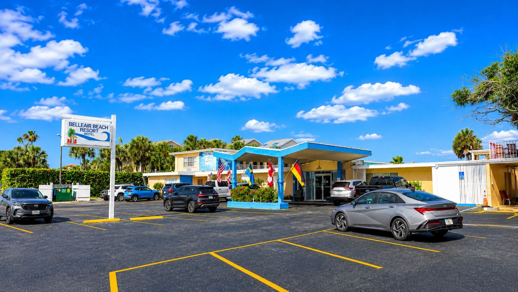 A motel with a sign, a parking lot, and a building with flags.