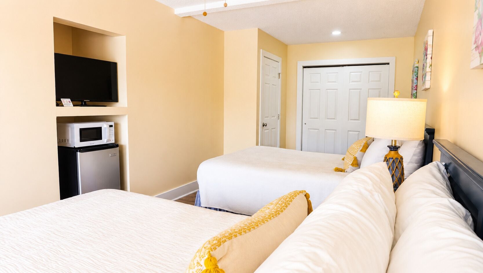 A hotel room with two beds, a television, a microwave, and a door.