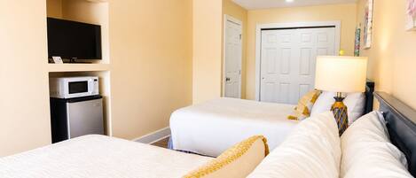 A hotel room with two beds, a television, a microwave, and a door.