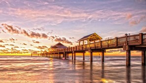 Un muelle de madera se extiende sobre aguas tranquilas, con bungalows sobre el agua y un cielo despejado.