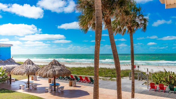 A beachside patio with thatched umbrellas, outdoor seating, and a view of the ocean.