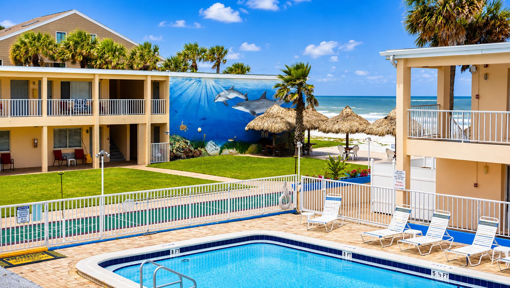 Un hotel con piscina, sillones de descanso y un mural de delfines.
