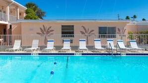 A swimming pool with lounge chairs and a building with palm tree murals.