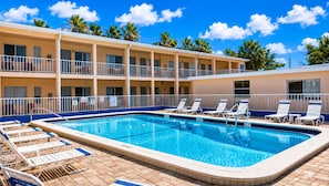 Un hotel con piscina, varios balcones y sillones de descanso.