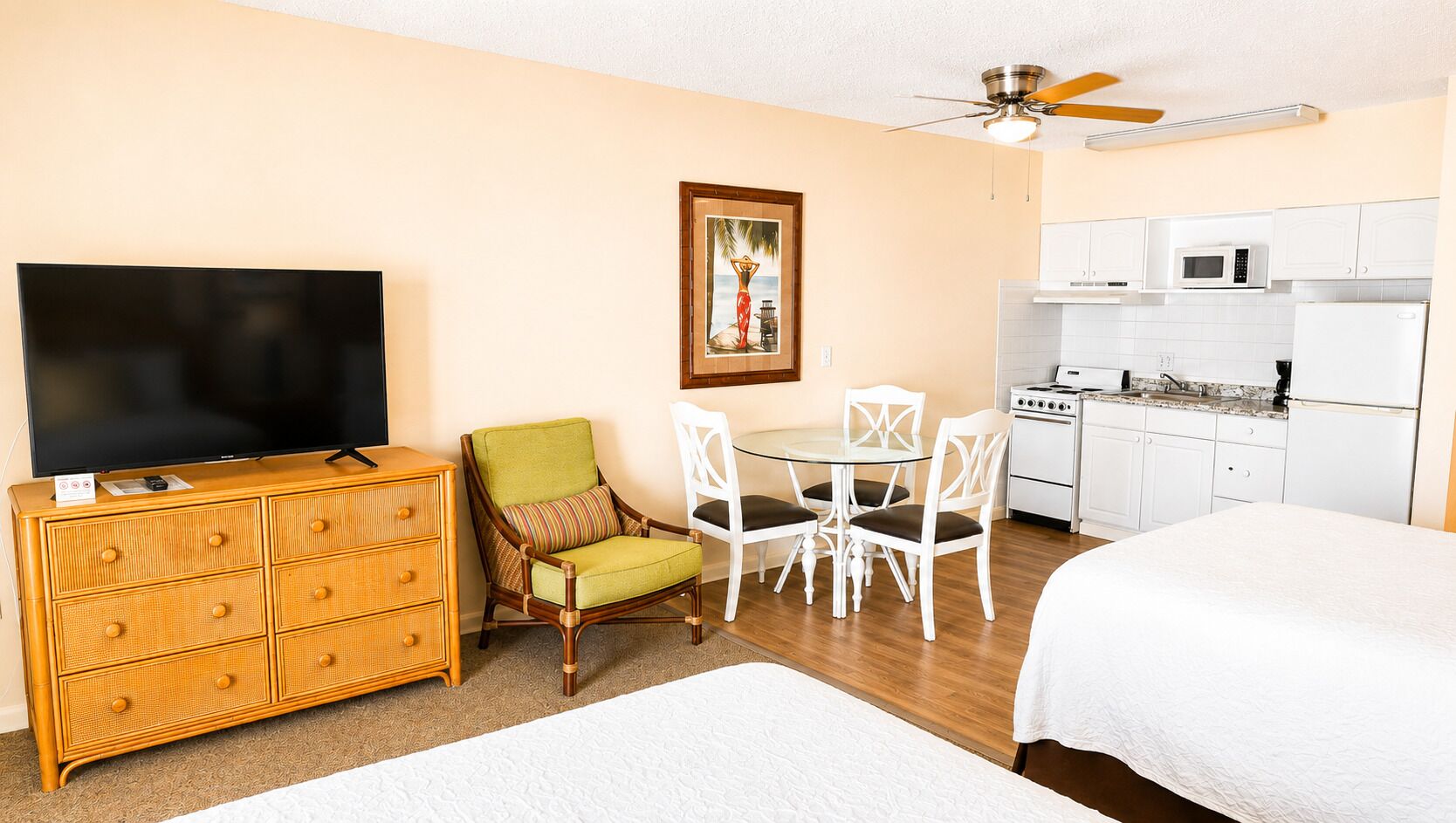 A hotel room with a TV, a dining table with chairs, a kitchenette, and a bed.