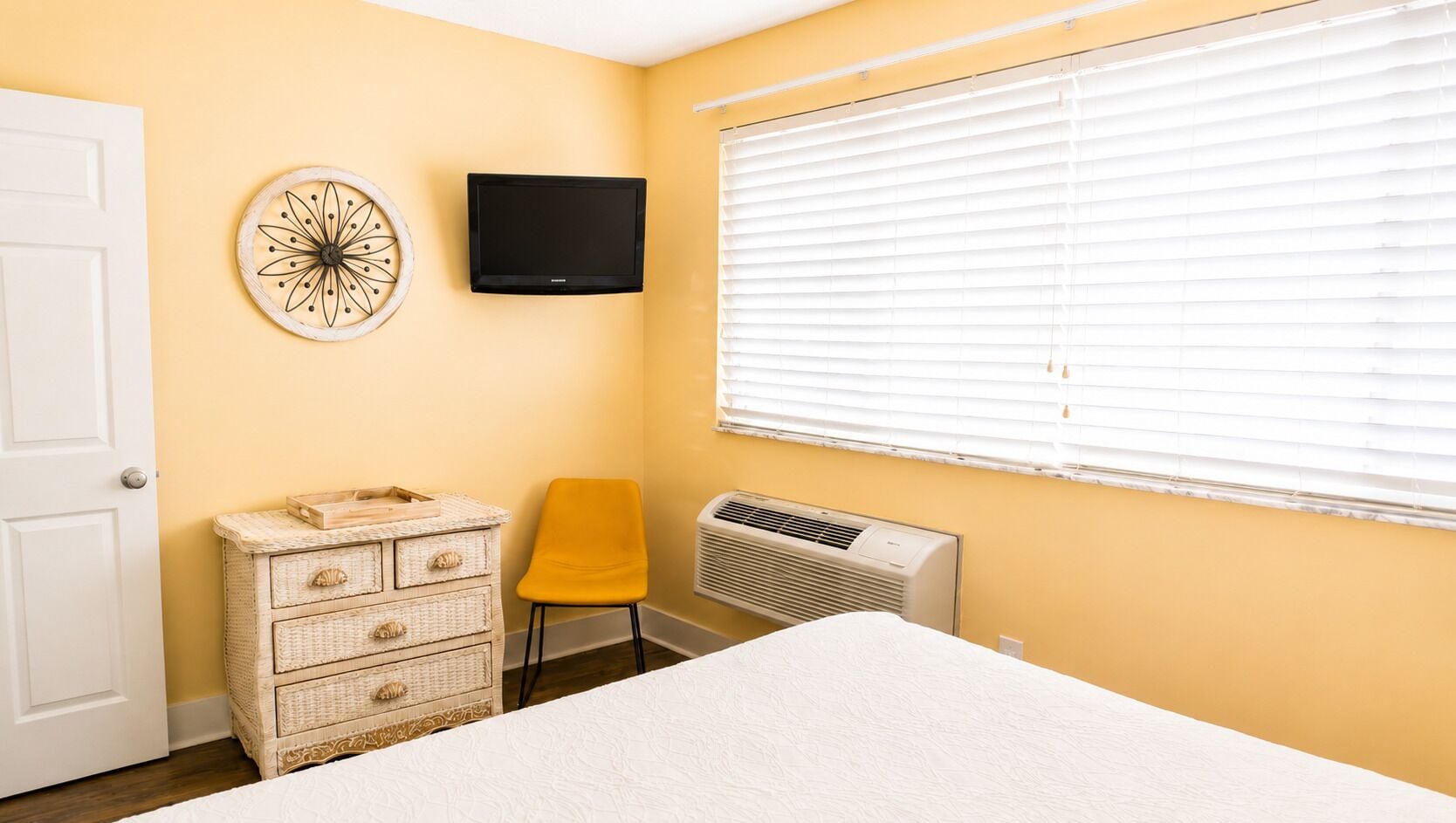 Un dormitorio con cama, cómoda, silla, televisor montado en la pared y aire acondicionado.