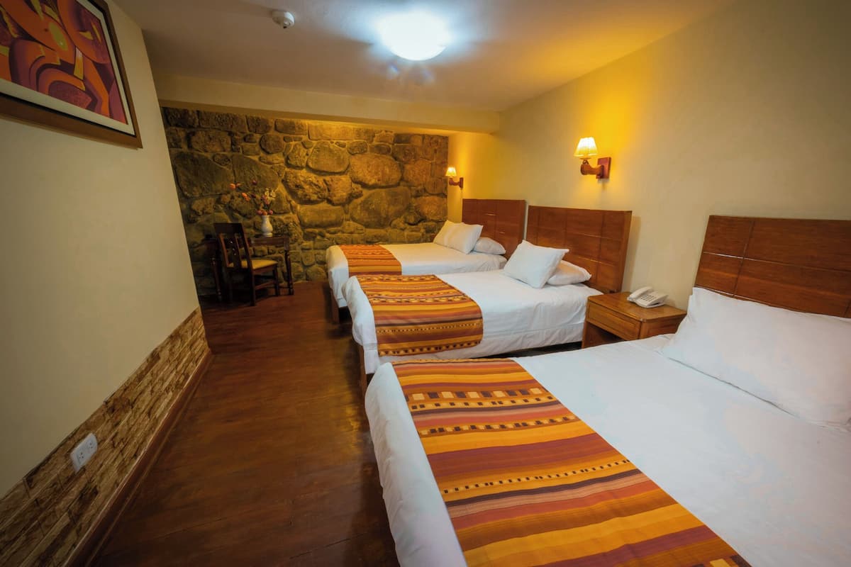 Ein Hotelzimmer mit drei Betten, einer Steinwand, einem Holzboden und einem kleinen Tisch mit Stühlen.