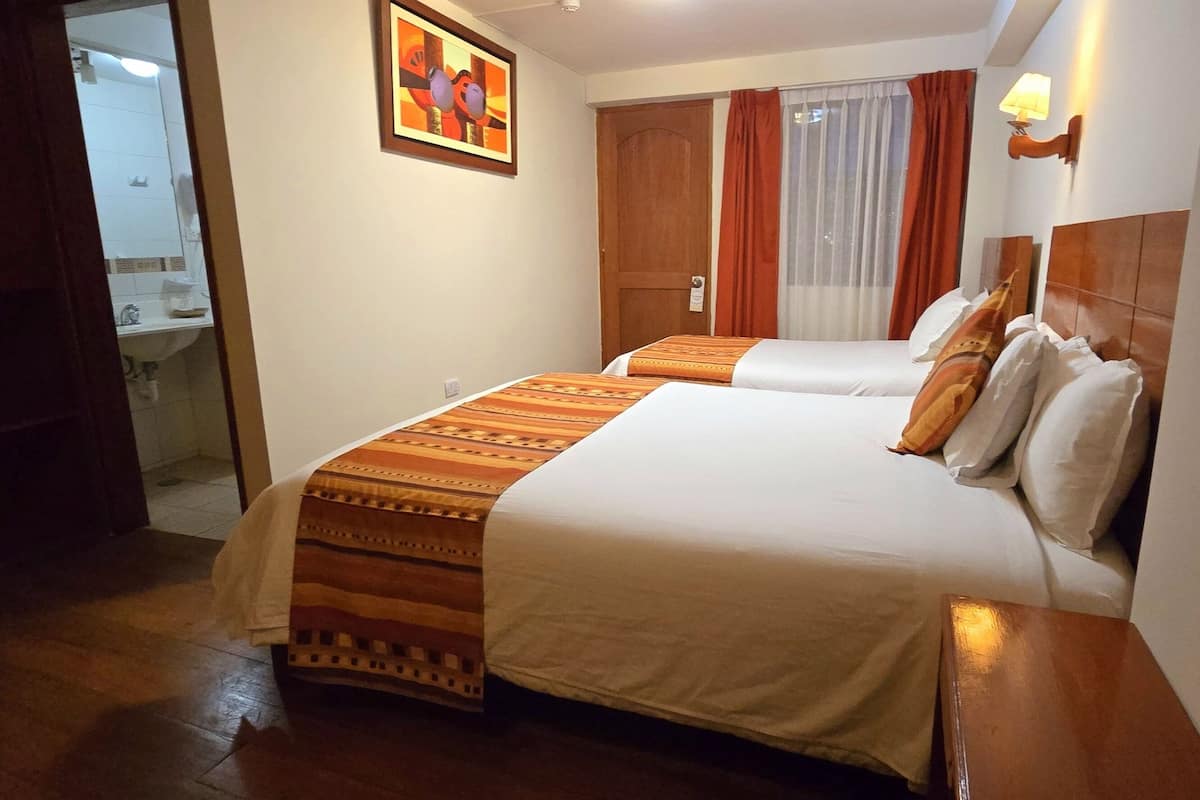 Ein Hotelzimmer mit zwei Betten, einem Holzschrank, einem durchgehenden Türrahmen einsehbarer Badezimmers und einem Bild an der Wand.
