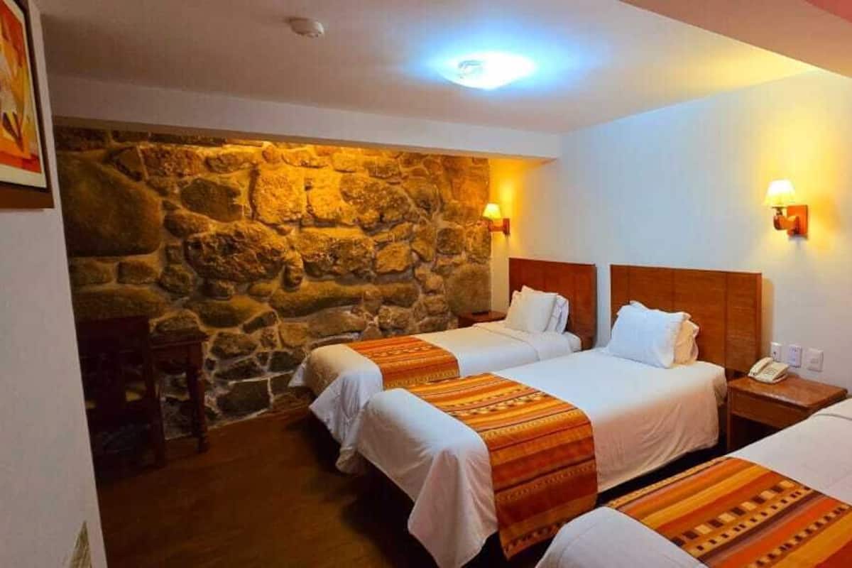Ein Hotelzimmer mit drei Betten, einer Steinwand und zwei Wandlampen.