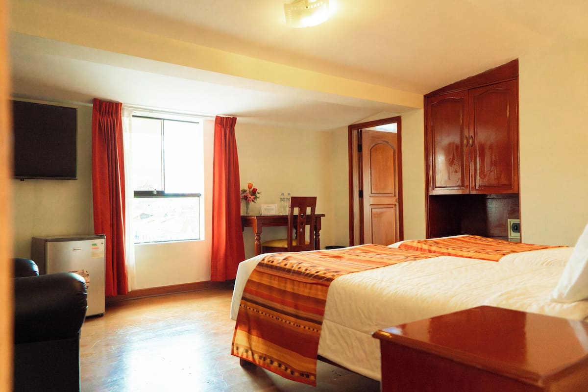 Ein Hotelzimmer mit Bett, Schreibtisch, Stuhl, Fernseher und einem fenster mit Vorhängen.