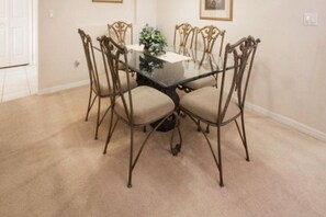 A dining area with a glass-top table surrounded by four chairs with metal frames and beige cushions. - Highlands Reserve Villas (Davenport)